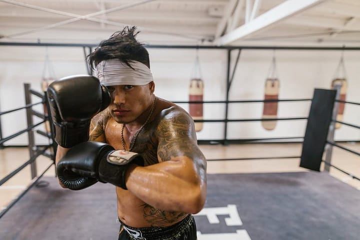 Shirtless man wearing black boxing gloves and a white bandanna