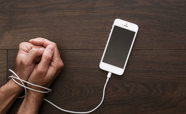 Hands tied by a charging smartphone’s cable