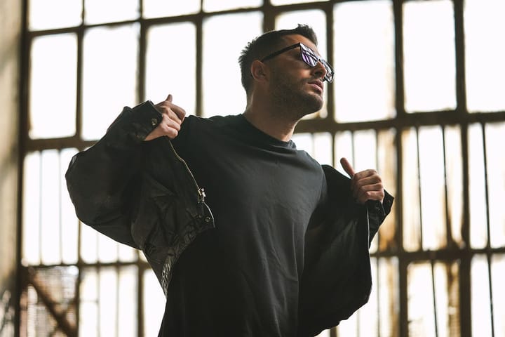 Man in a black shirt with black shades shrugging off a black jacket