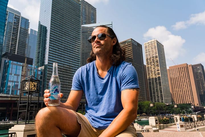 Man with aviators sitting with a water bottle in the backdrop of a city line