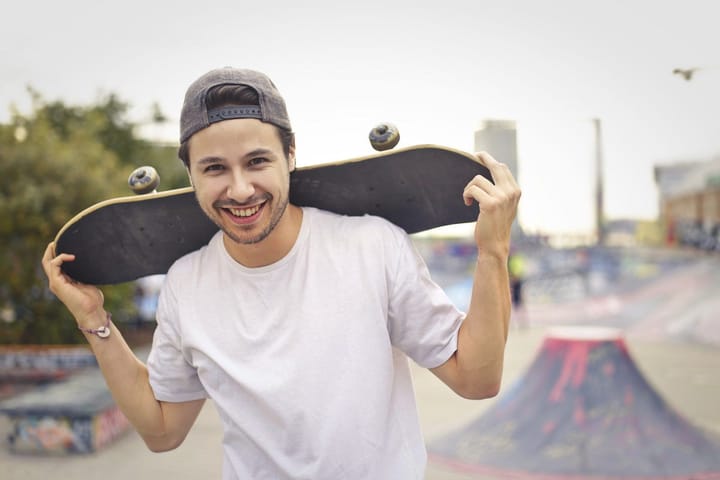 Smiling man with a reversed cap with a skateboard on his shoulders