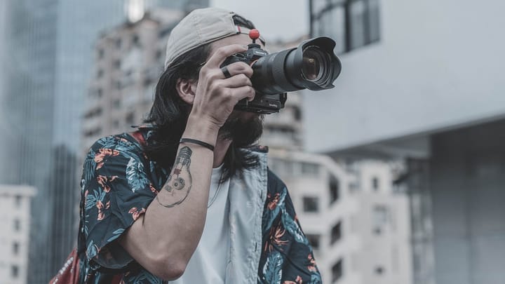 Man with a forearm tattoo and long hair holding a DSLR