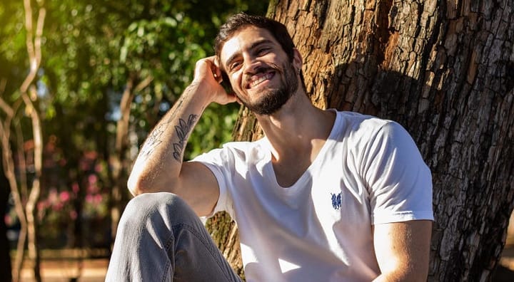 Smiling young man with a tattoed forearm sitting in the sun