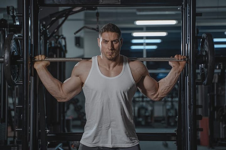 Muscular young man posing in a tank top with the smith machine