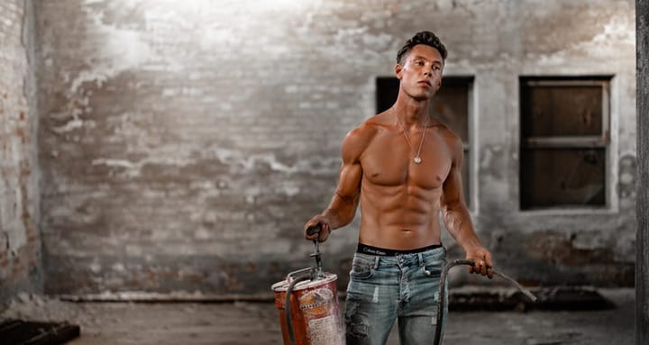 Shirtless tanned white man in jeans carrying a fire extinguisher