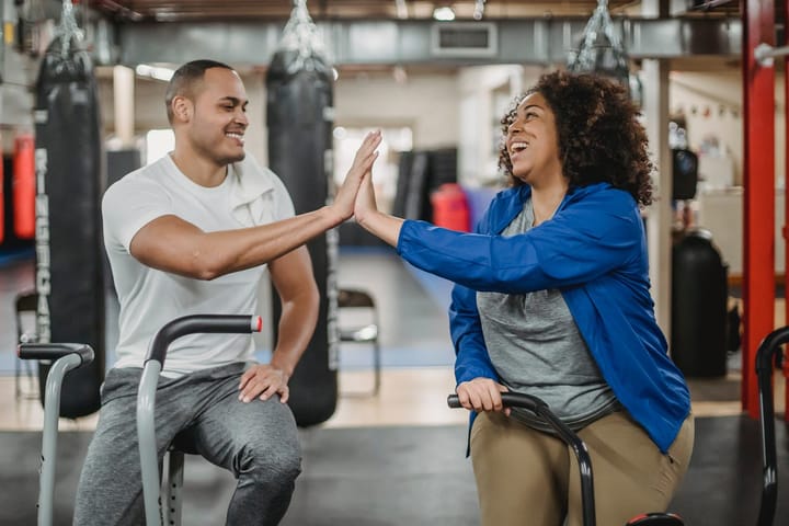 Joyful diverse trainee and fitness instructor clapping hands in gym