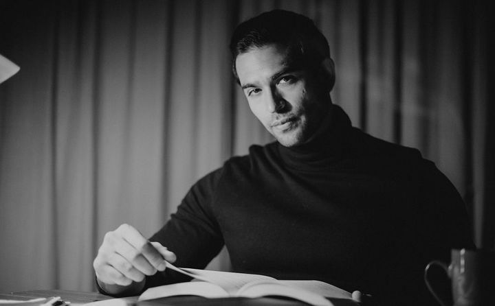 Black and white photo of a young thoughtful man in a black full-sleeved shirt reading a book