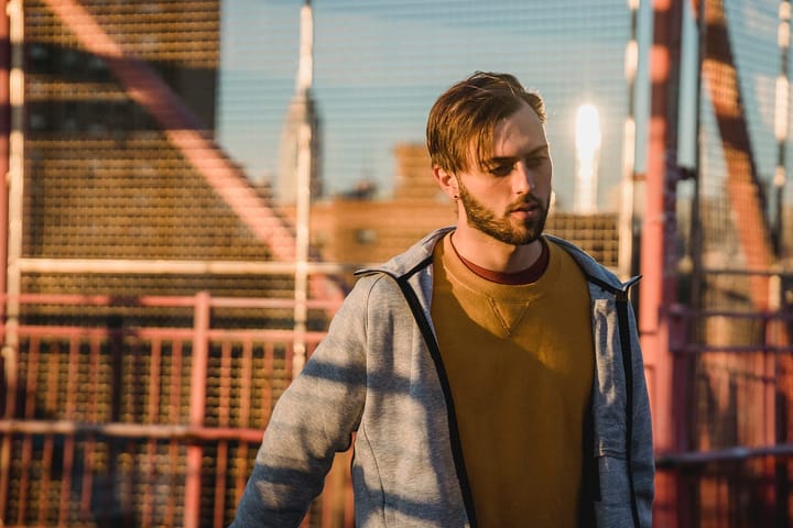 Man with brown hair wearing a denim jacket and a yellow shirt in the backdrop of a sunny day