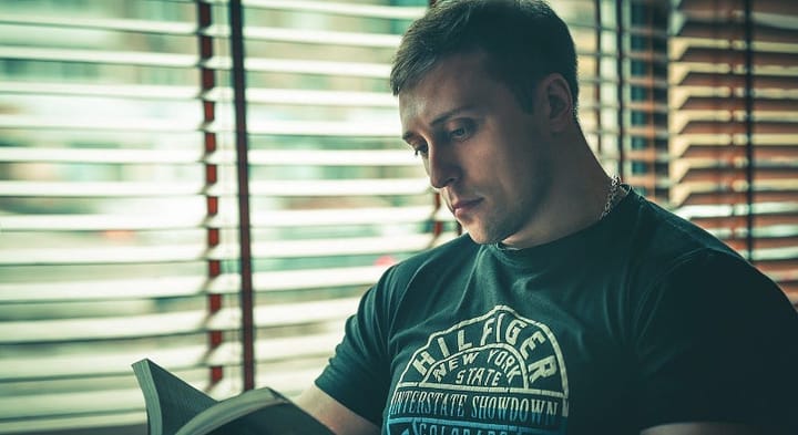 Muscular young man reading a book beside a shuttered window