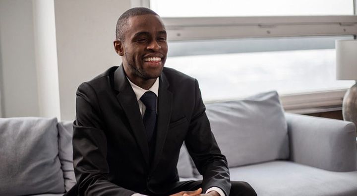 Handsome, formally dressed, smiling black man sitting on a sofa