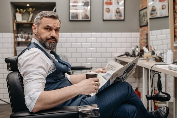 Stylish old man sitting with a newspaper and a cup of coffee in a salon