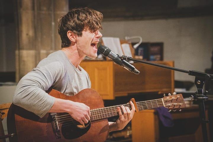 Muscular dude in a grey shirt playing the guitar