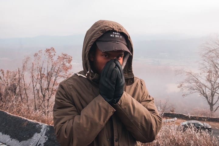 Black man in an Autumn weather clasping his mittens to his face