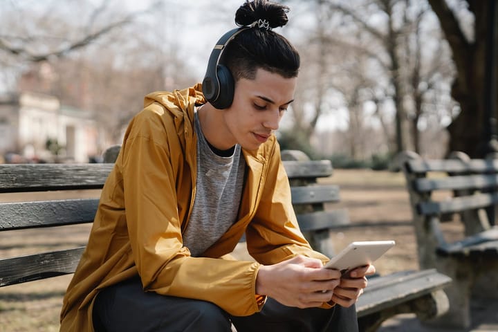 Man in a brown sweater sitting on a bench looking at his tab