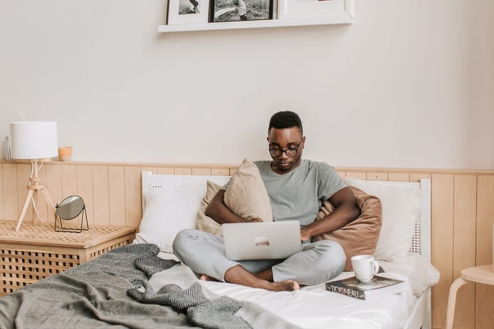 Black man sitting in a disheveled bed with his laptop