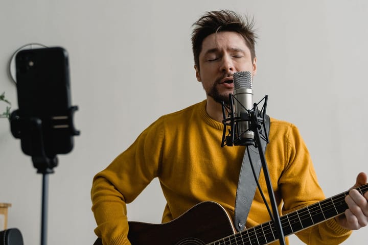Man in a yellow-orange sweater singing with a guitar