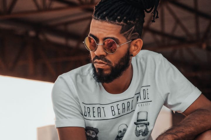 Still of a man with a beard, fancy hairdo, and stylish shades
