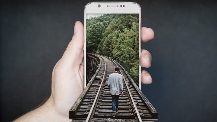 Surreal image of a man walking on a rail road into a smartphone