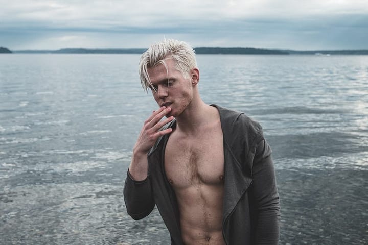 Blonde haired fit man with his shirt undone by the beach