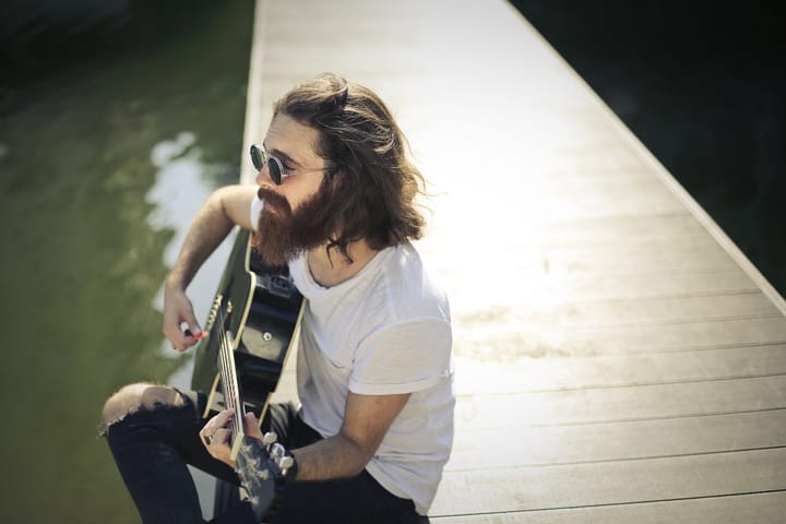 Man with long hair and shades sitting with a guitar alone