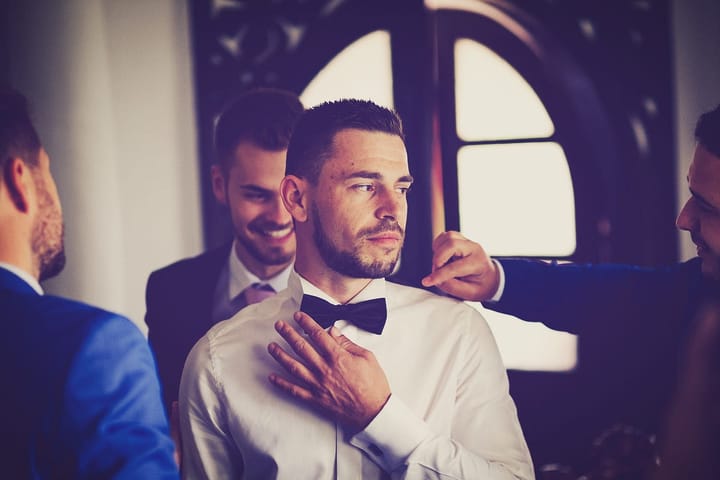 A man in a wedding suit looking aside while surrounded by friends
