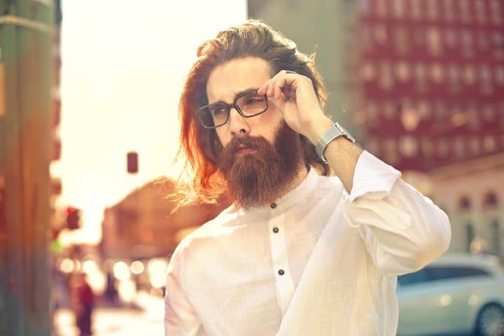 Stylish man in a white buttoned shirt with a full beard, long hair, and spectacles