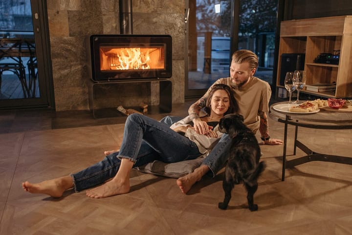 A couple with their dog sitting by the fireplace during a snowy late evening