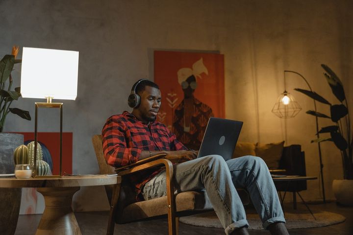 African man wearing a red checkered shirt in a lamp-enlightened room using his laptop