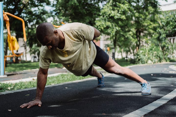 Black man in a light yellow shirt doing a one arm pushup