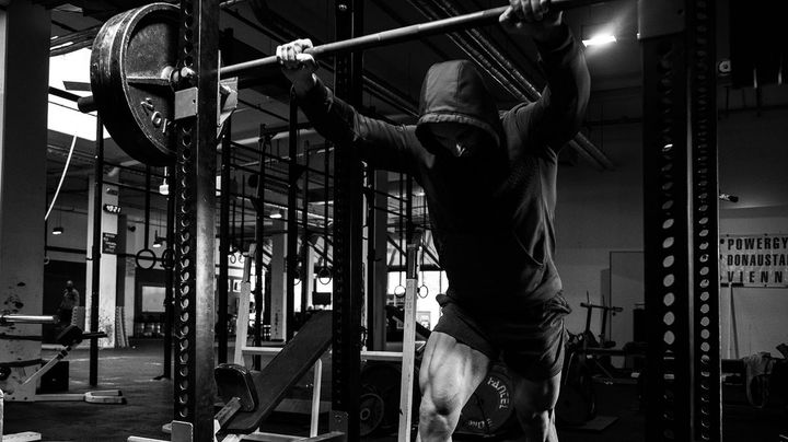 Muscular hooded man in the squat rack